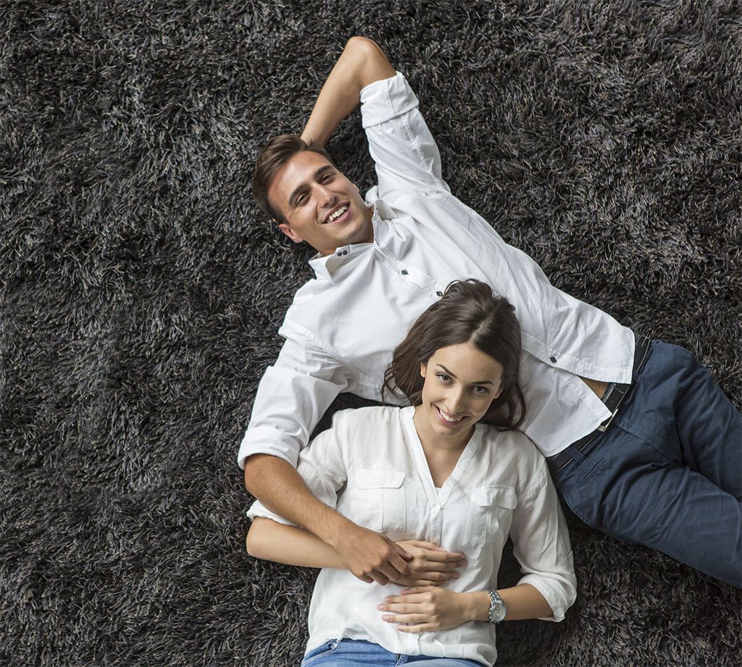 Zwei Personen in weißen Hemden liegen auf einem grauen Zottelteppich
