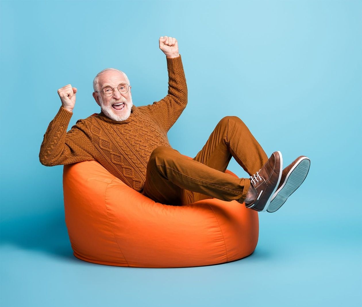 Person in einem braunen Pullover, die mit erhobenen Fäusten auf einem orangefarbenen Sitzsack sitzt