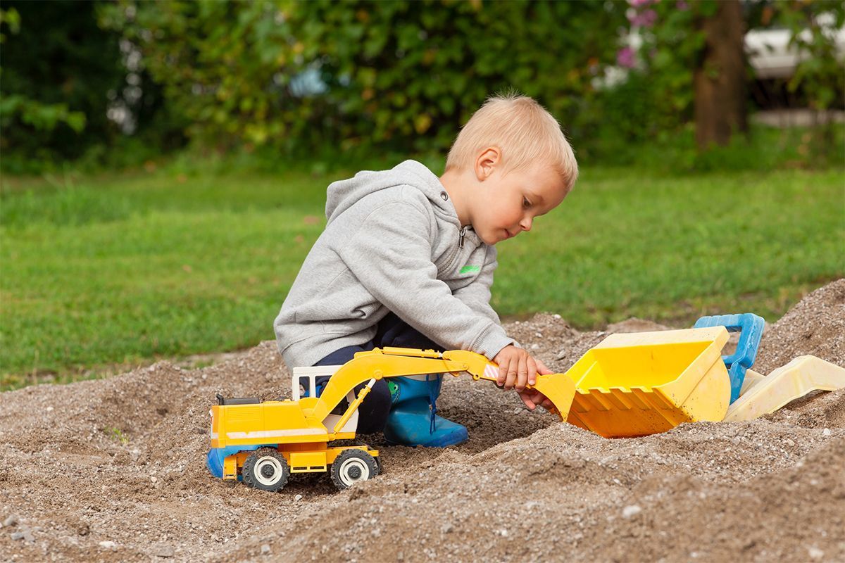Kind spielt mit einem Bagger im Sand
